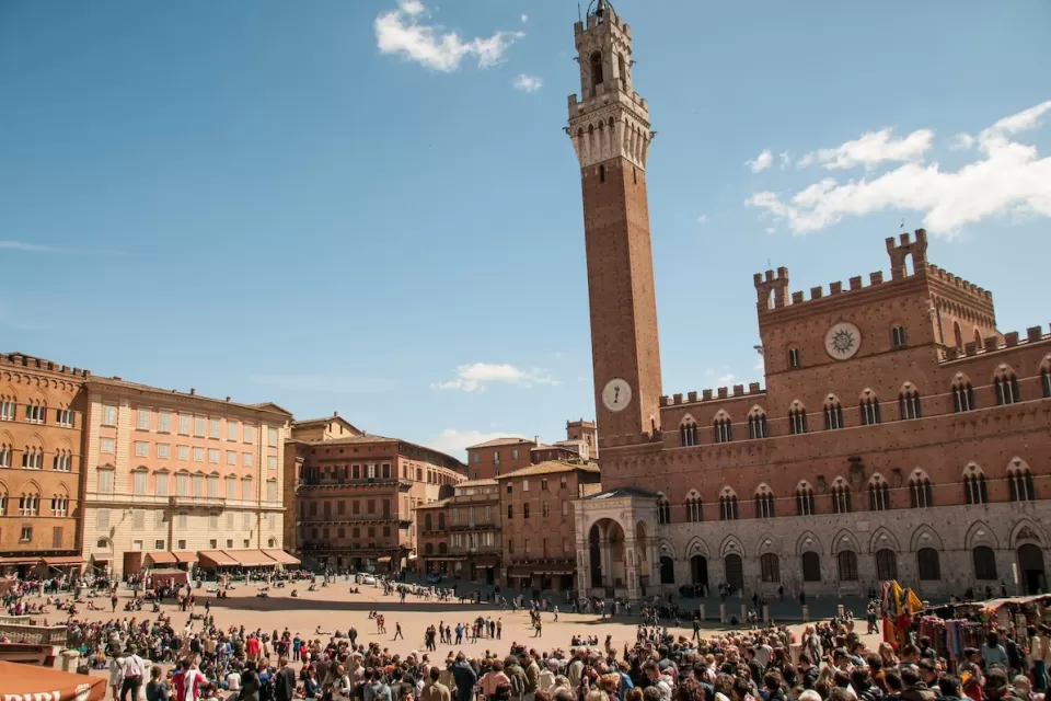 Busy plaza in Siena, Italy with prominent clock tower.